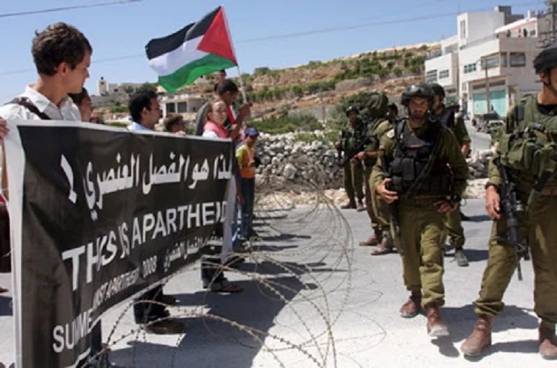 Civilians held behind concertina wire facing armed soldiers